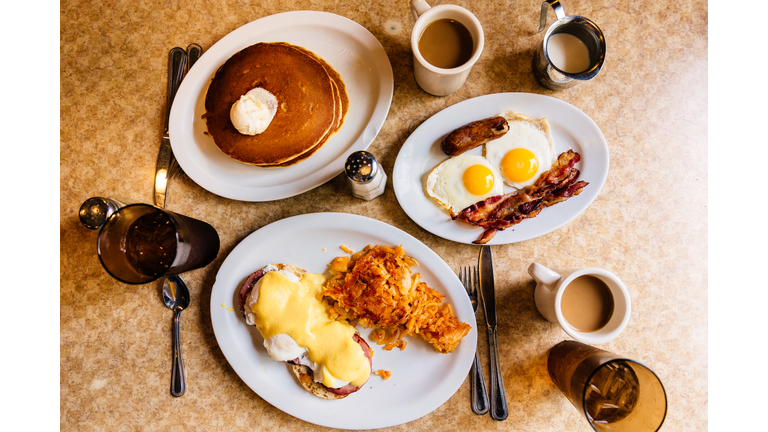 Pancakes, fried eggs with bacon and Eggs Benedict with ham and hash brown served at a traditional American diner, high angle view