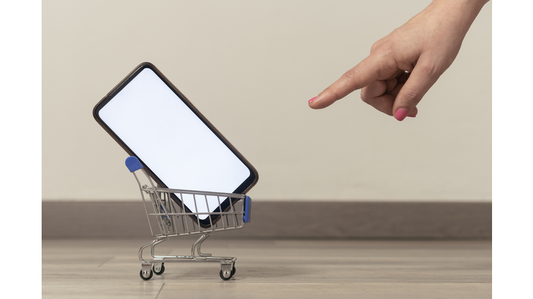 Ecommerce concept image: woman pointing a cart with a blank screen smartphone inside