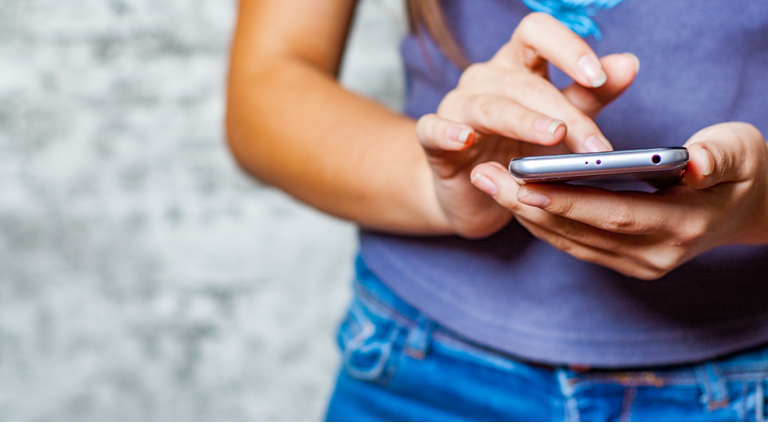 young teenager girl hand using mobile phone or smartphone on gray wall background