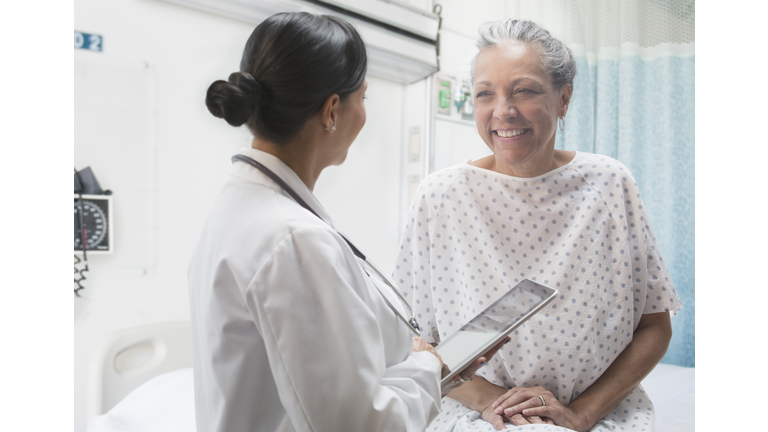 Hispanic doctor using digital tablet and talking to older patient
