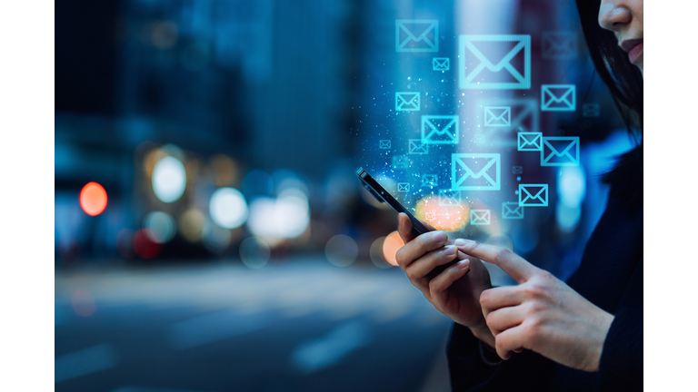 Close up of young Asian woman sending email with smartphone in the city, against illuminated city street lights in downtown district. Information technology concept