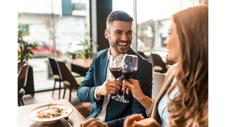 Happy couple eating lunch together in a restaurant and toasting with wine.