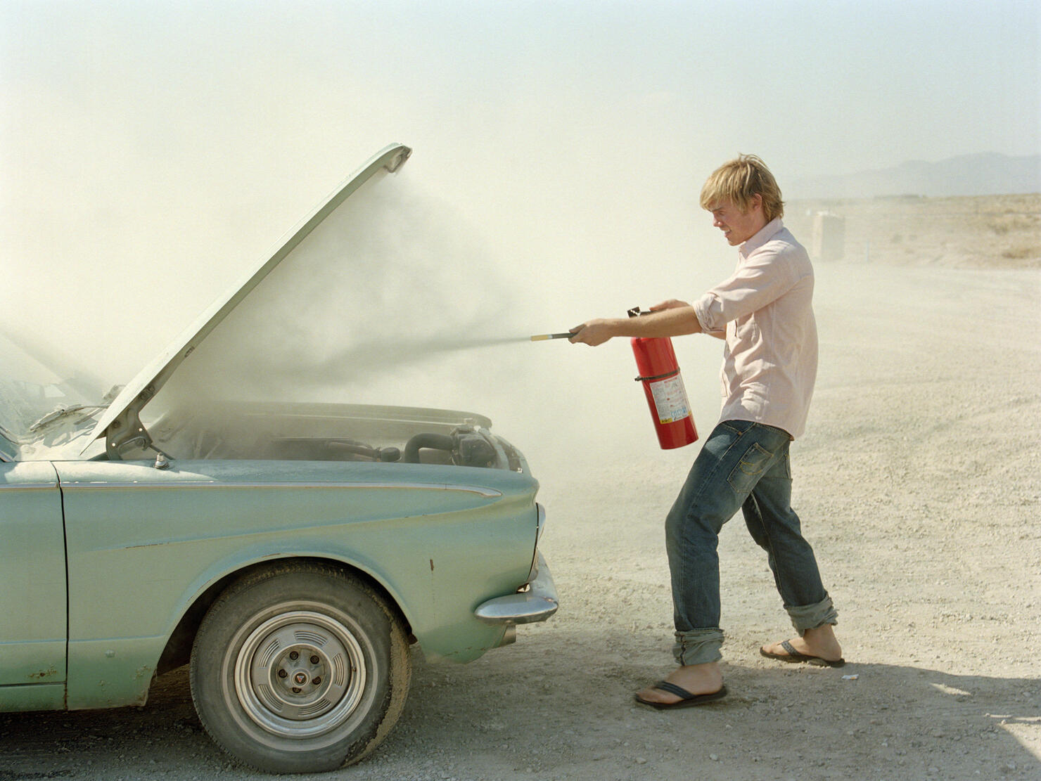 Young man spraying fire extinguisher in car hood