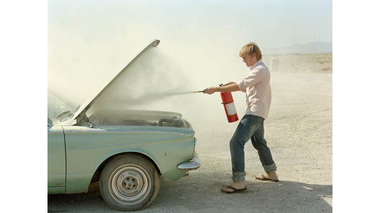 Young man spraying fire extinguisher in car hood