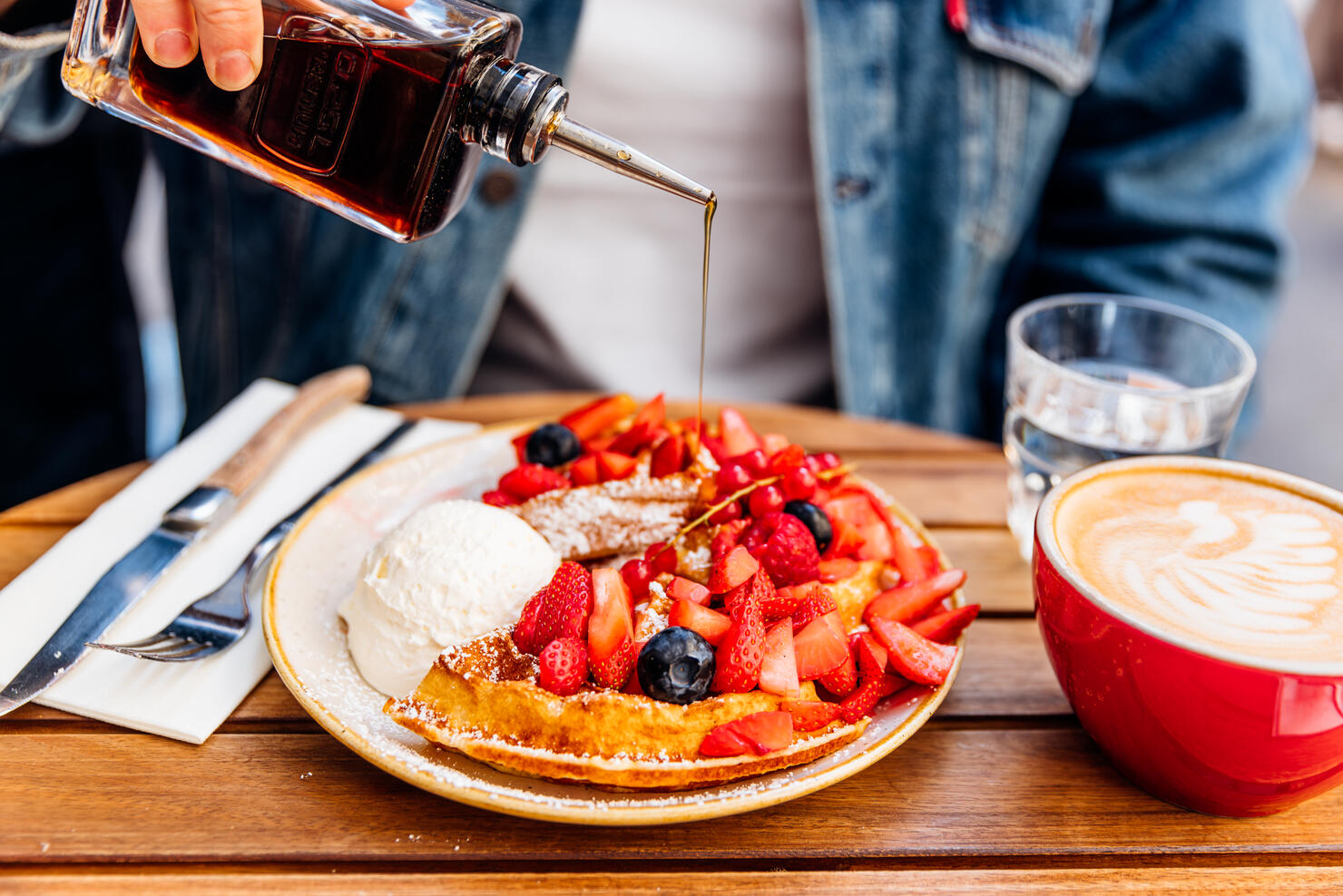 Man pouring maple syrup on waffles with fresh berries and ice cream