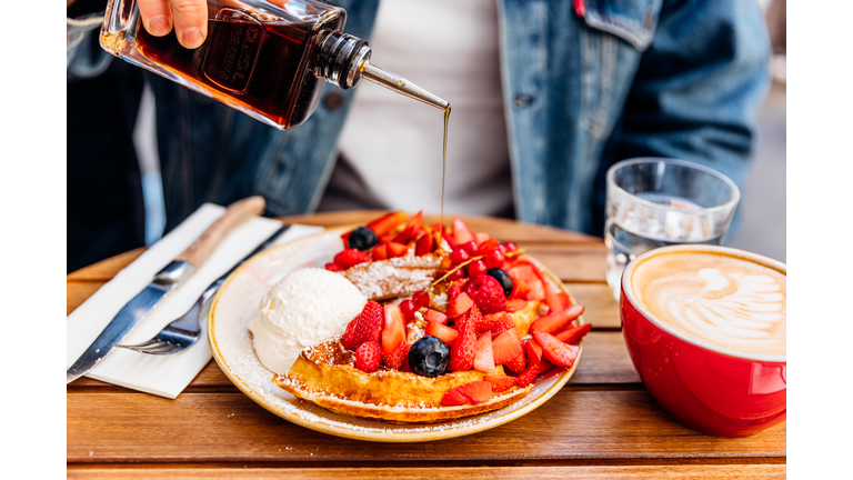 Man pouring maple syrup on waffles with fresh berries and ice cream