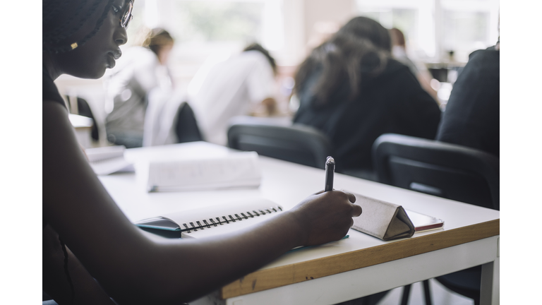 Teenage student writing in book on desk at junior high school
