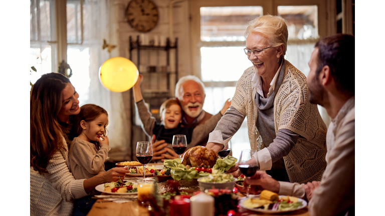 Happy senior woman serving a meal to her family in dining room.