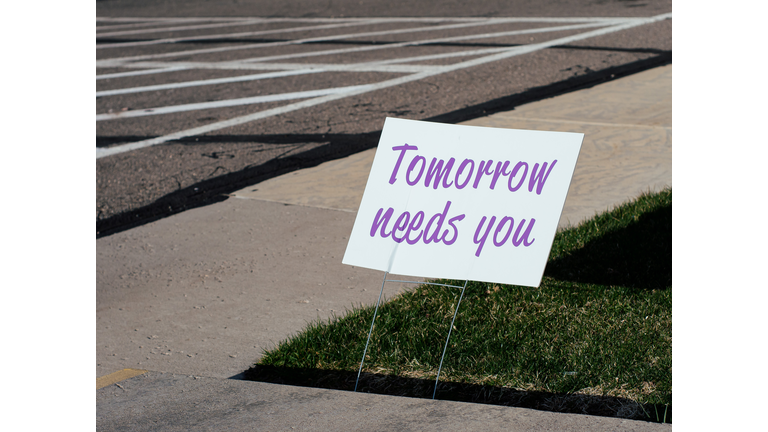 Sign that reads "Tomorrow needs you" placed by a sidewalk.