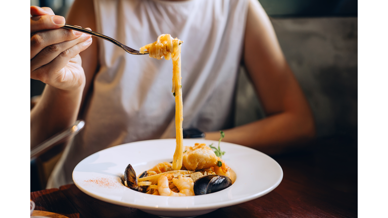 Cropped shot of young woman eating fresh seafood pasta in restaurant during vacation. Exploring authentic cuisine. Travelling, food and lifestyle