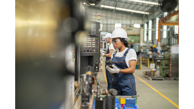 Female apprentice engineer working with CNC machine in factory