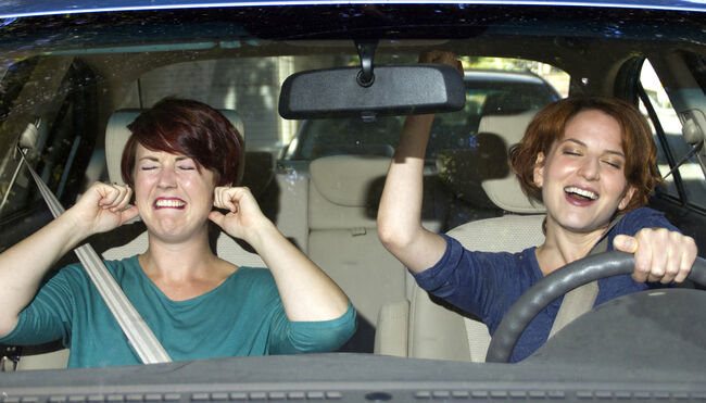 One woman singing and one woman covering her ears in a car