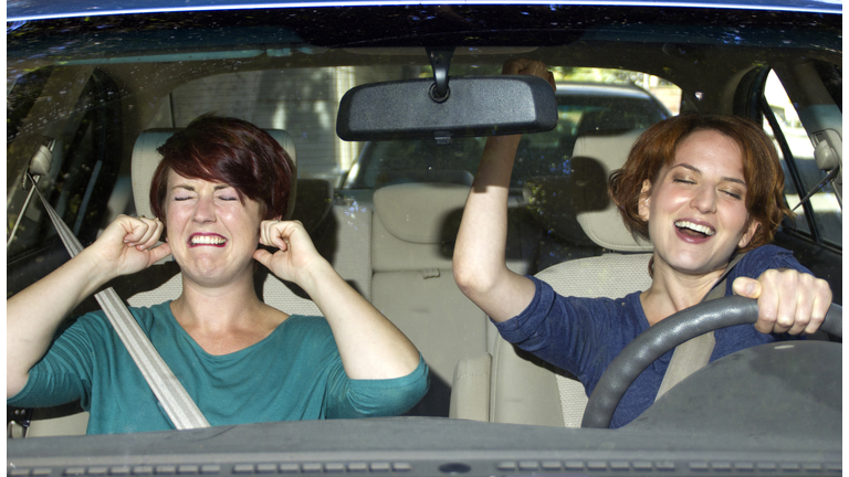 One woman singing and one woman covering her ears in a car