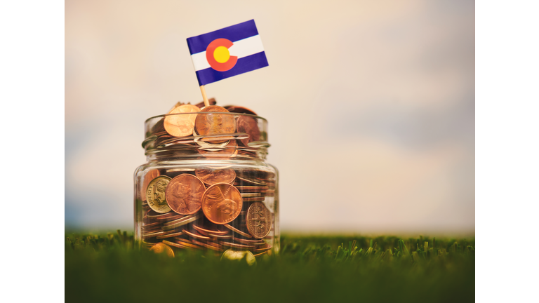 Savings jar filled with American currency with a Colorado flag