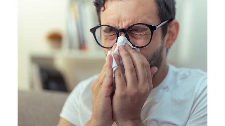 Young man sneezing, wiping his nose with a piece of tissue paper