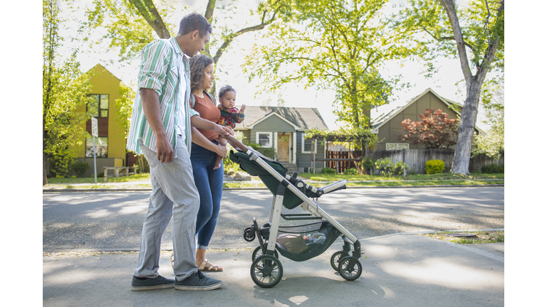 Young family with baby daughter walking on neighborhood street