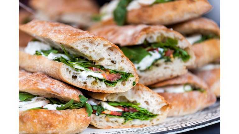 Closeup of fresh display of stacked pile of panini bread, mozzarella melted cheese, vegetarian italian tomatoes, basil lettuce in store, shop, cafe buffet catering sandwiches