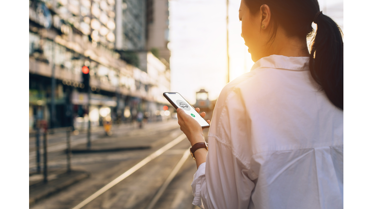 Young woman using mobile app on smartphone to arrange transportation ride in city street at sunset