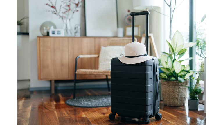 Still life of a black suitcase with a straw hat in the living room of an apartment. Travel and vacation concept