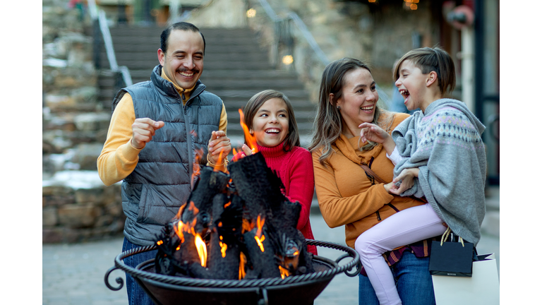 Hispanic family laughing around fire pit in a luxury mountain ski town.