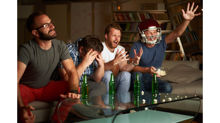 Four friends watching american football game on television, feeling frustrated