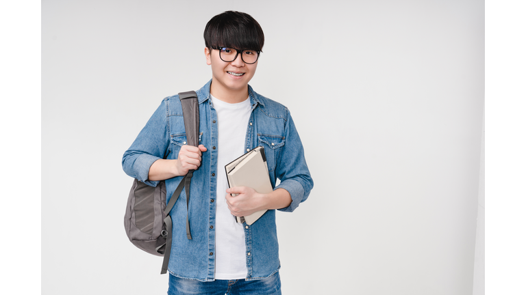 Smiling with braces young asian korean smart man student high schoolboy holding textbooks and notebooks, carrying a bag, going to university school college isolated in white background