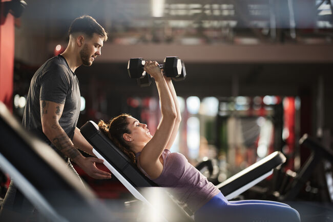 Young man helping his girlfriend during her sports training in a health club.