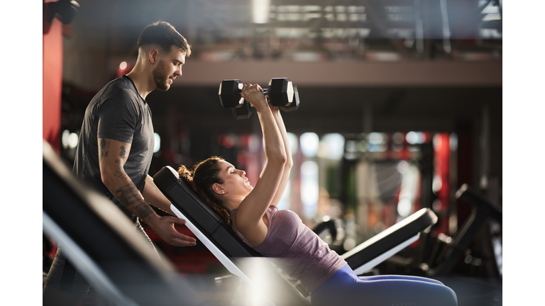 Young man helping his girlfriend during her sports training in a health club.