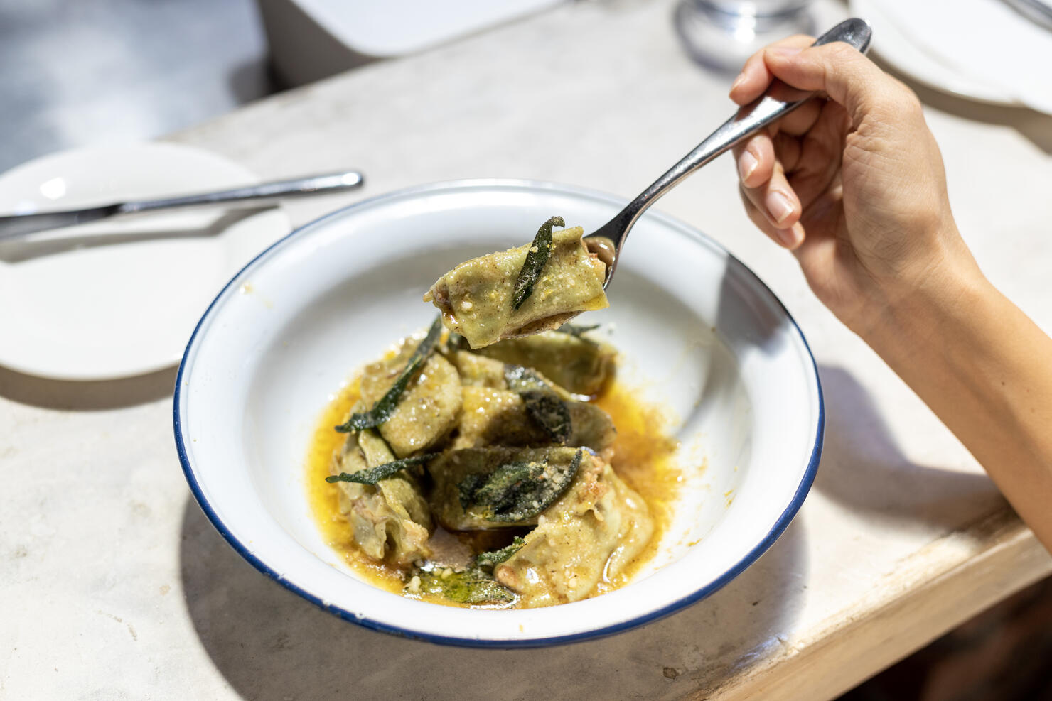 Cropped image of woman enjoying eating spinach agnolotti filled with mortadella & ricotta with lemon zest butter sauce in a restaurant