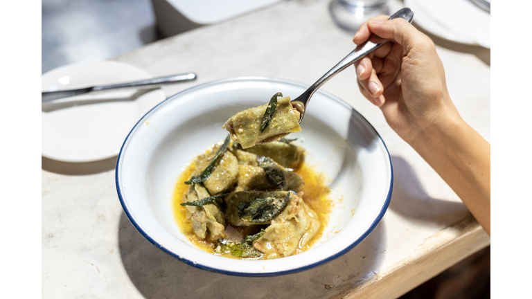 Cropped image of woman enjoying eating spinach agnolotti filled with mortadella & ricotta with lemon zest butter sauce in a restaurant