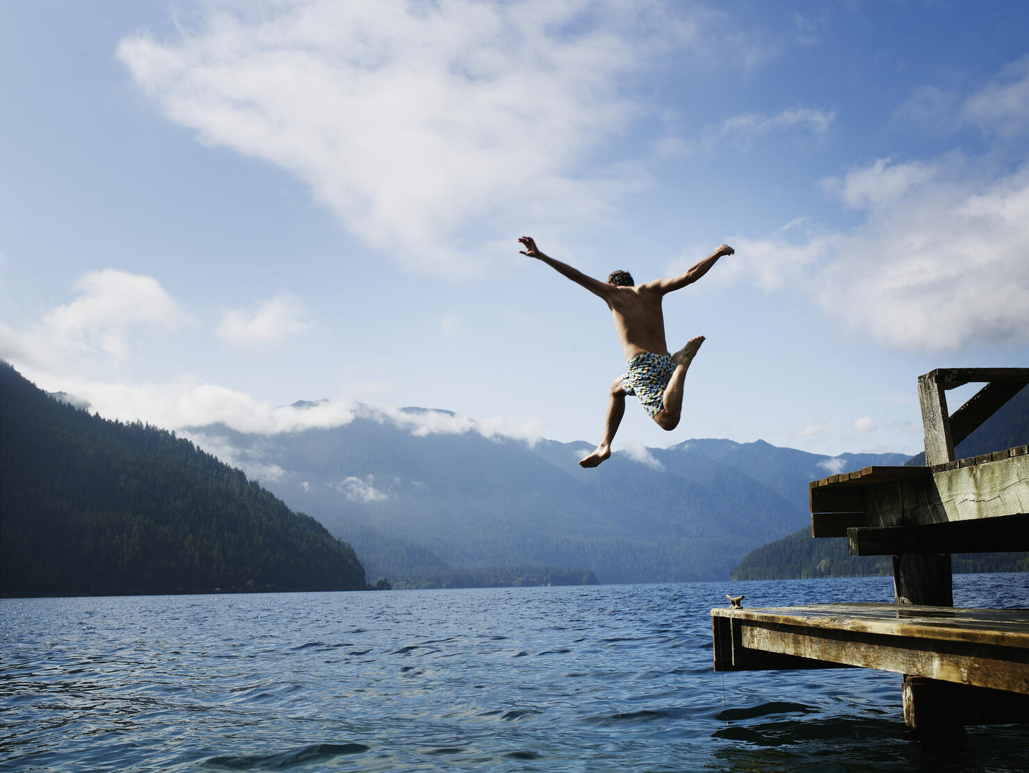 Young male jumping off dock into lake in mid air