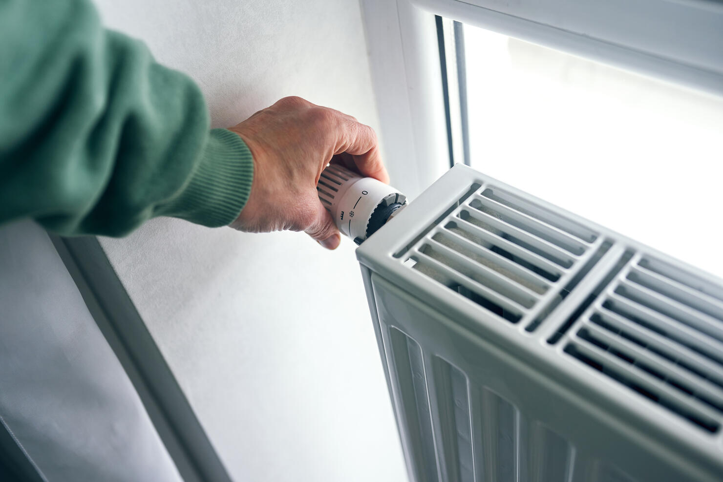 Close-up of female hands regulating the thermostat on the radiator.