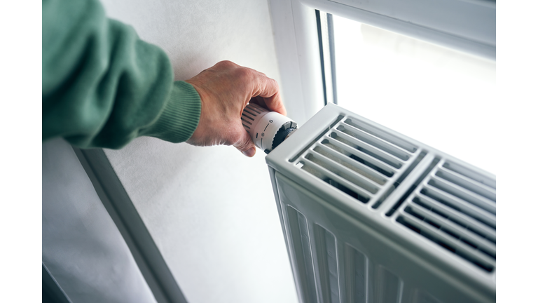 Close-up of female hands regulating the thermostat on the radiator.