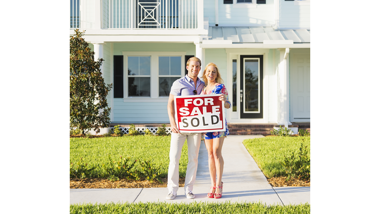 Caucasian couple holding sold sign outside new home