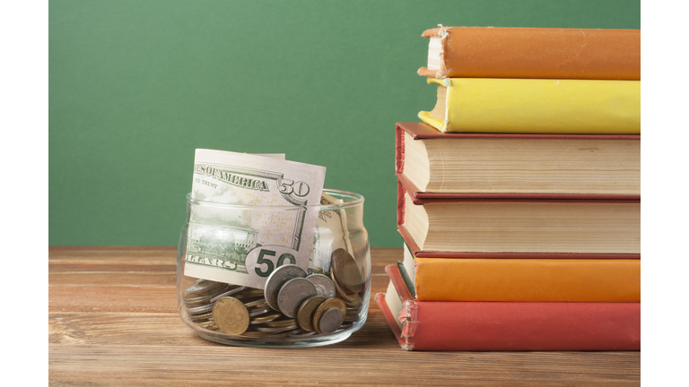 Coins in glass jar and stack of books on wooden table.Saving,financiai and education concept.