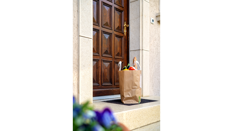 Contactless food delivery service concept. Paper bag with groceries delivered and left outside at doorstep. Shopping online. Healthy fresh fruit and vegetables, zero waste, recyclable package. Side view