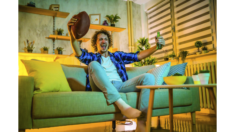 Young happy man watching American football on TV