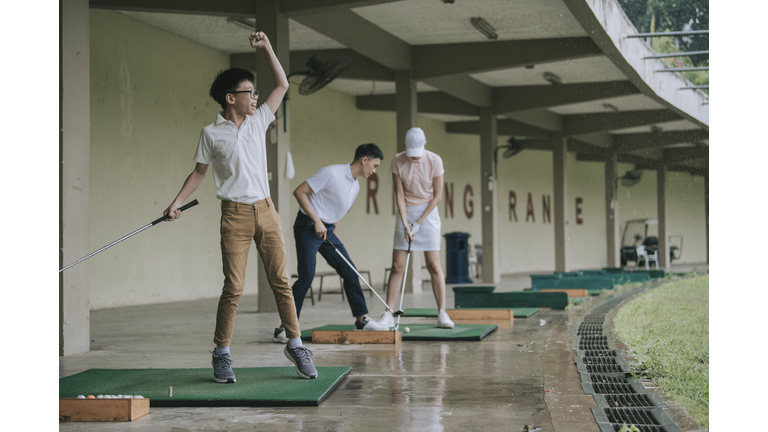 Asian chinese young boy practicing golf in driving range with his parents during raining