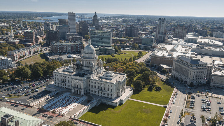 Rhode Island State House in Providens on Capitol Hill, famous landmark of the city, with a remote view of Downtown Providence and Providence River in the backdrop.