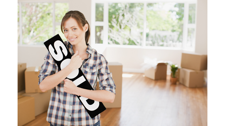 Woman holding sold sign in her new house