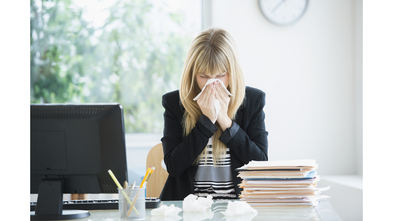 Businesswoman blowing nose in office