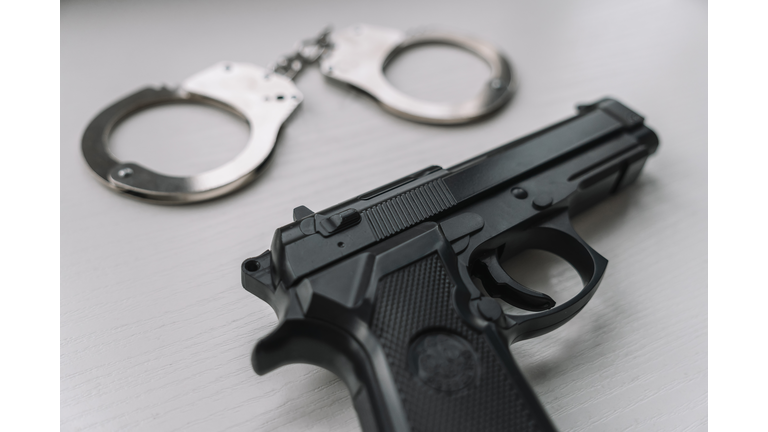 Arrest concept. Black handgun gun with handcuffs on wooden surface