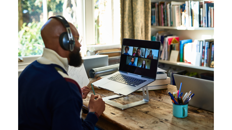 Black entrepreneur wearing headphones on video conference call on laptop in home office