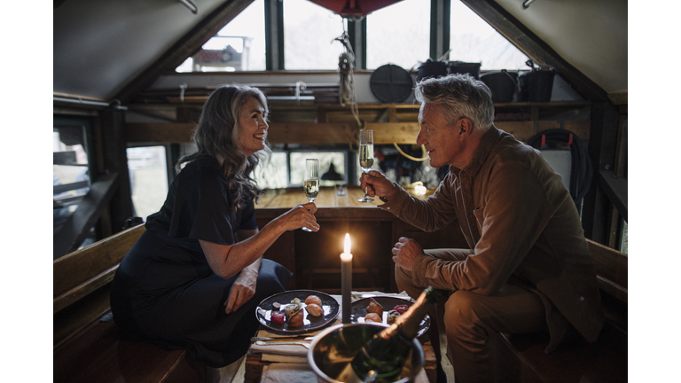 Senior couple having a candlelight dinner on a boat in boathouse clinking champagne glasses