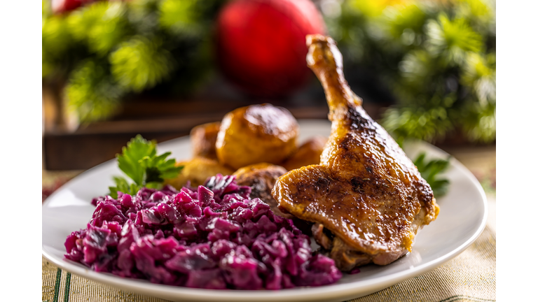 Duck or goose leg served with red cabbage and baked potatoes on a festive Christmas decorated table.