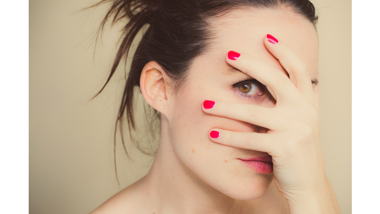 Misterious girl with red nails and hand on face.