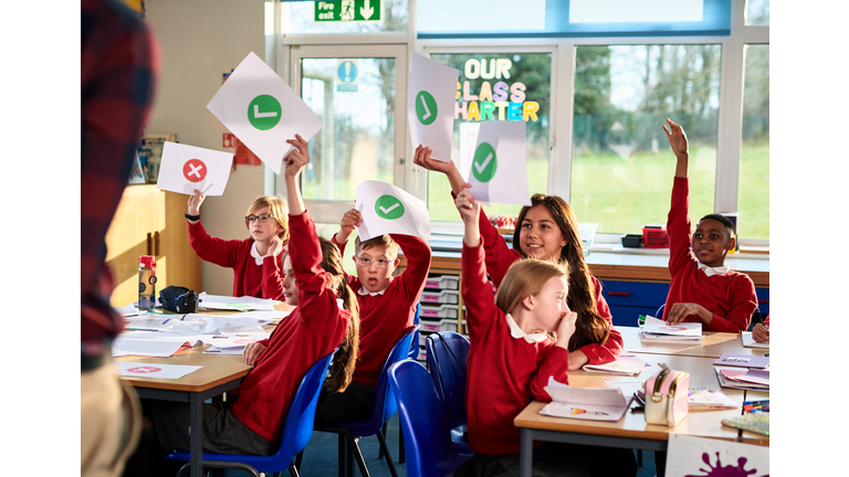 Primary school class holding up pieces of paper, classroom discussion, making decisions, voting