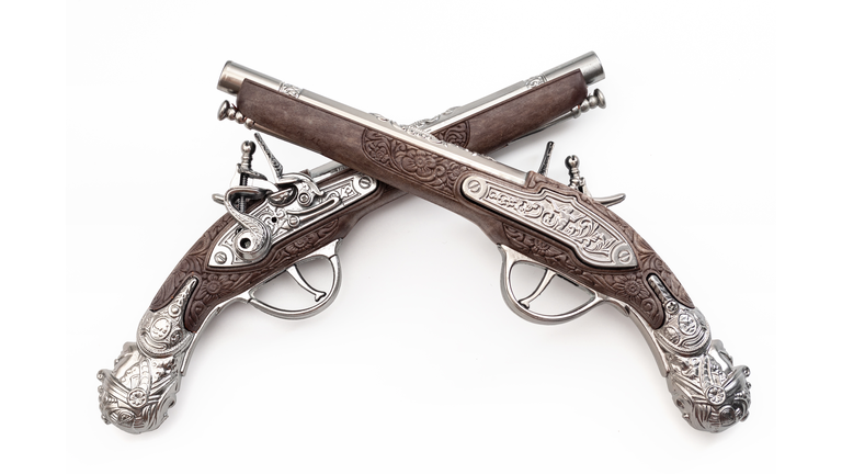 Firearms dating to the American revolution and antique collectables concept with ornate old fashioned dueling flintlock pistols crossed in duel isolated on white background with clipping path cutout