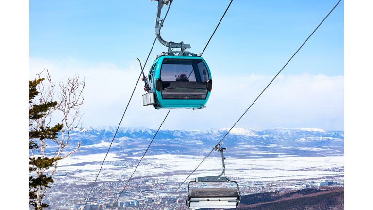 Cable car cabin with the skiers and snowboarders against the snow covered mountains and city