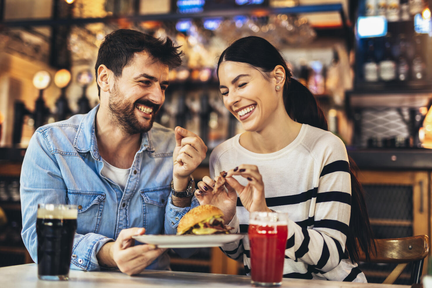 Young couple eating burgers and drinking beer